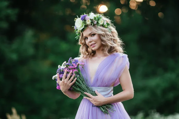 Schoonheid vrouw portret met krans van bloemen op hoofd. bruid in paarse jurk met boeket van wilde bloemen. Buiten. Soft Focus Sea... — Stockfoto