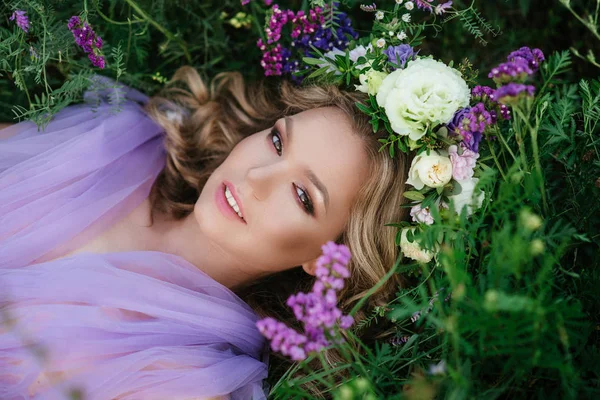 Portret model piękna dziewczyna, leżąc na trawie. Panna Młoda w wieniec z purpurowe kwiaty. Od góry. — Zdjęcie stockowe