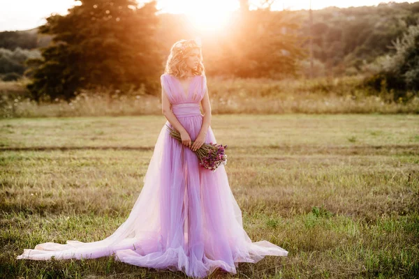 Schoonheid vrouw portret met krans van bloemen op hoofd bij zonsondergang. bruid in paarse jurk Outdoor. Soft Focus Sea... — Stockfoto