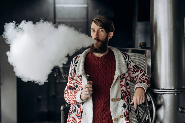 Joven con barba vapeando un cigarrillo electrónico al aire libre. vaporizador de humo hipster . — Foto de Stock