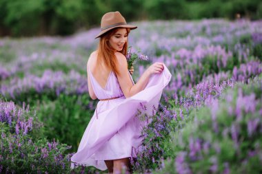 Şapkalı kızıl saçlı kız elinde mor çiçeklerle çimlerin üzerinde yatıyor. Genç bir kadın doğada gülümser. Bayan lavanta tarlasında yürüyor..
