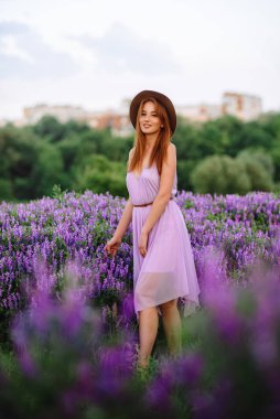 Şapkalı kızıl saçlı kız elinde mor çiçeklerle çimlerin üzerinde yatıyor. Genç bir kadın doğada gülümser. Bayan lavanta tarlasında yürüyor..