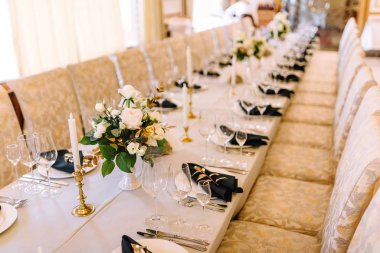 Restoranda şeffaf bardaklar, peçeteler ve tabak süslemeleriyle uzun bir düğün masası..