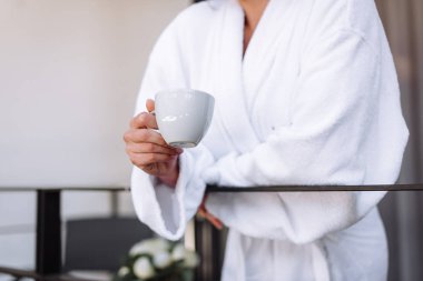 Beyaz bardak gelinin elinde, elinde fincanla balkonda bir kız.