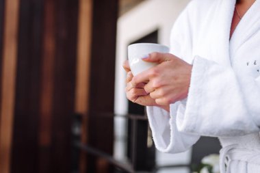 Beyaz bardak gelinin elinde, elinde fincanla balkonda bir kız.