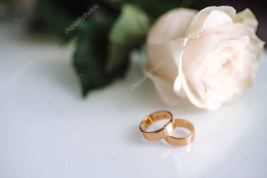 Close up of wedding ring on white table with white rose