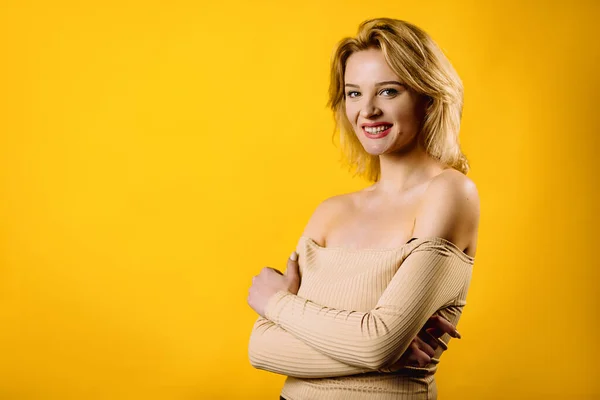 腕の中に立っている笑顔金髪の若い女性の肖像画は折り重ね黄色の背景分離 — ストック写真