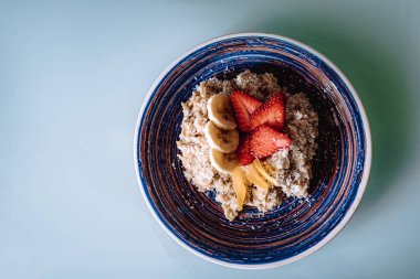 Çilekli yulaf ezmesi, muz balı ve mavi süslemeli hindistan cevizi gevreği. Sağlıklı organik yiyecekler. Mavi arka planda nefis bir kahvaltı. Yumuşak odak