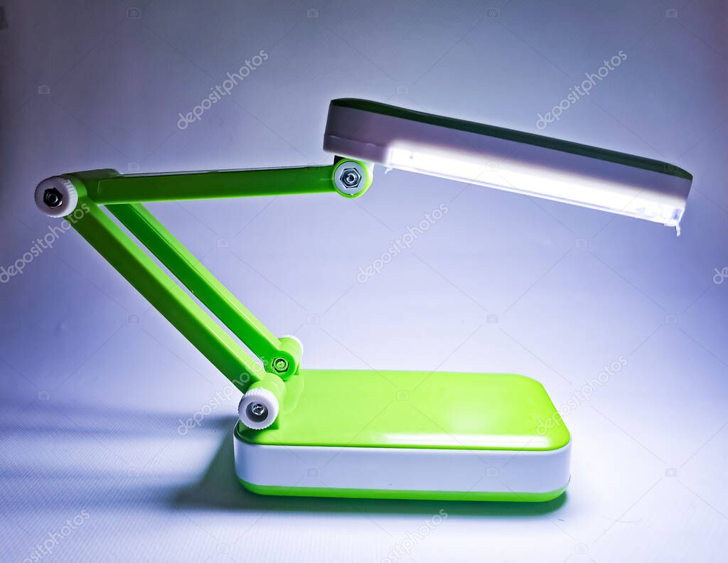 The LED table lamp is bright green. The lights of lamp are on in a poorly lit room. Image with noise effects.