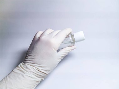 Beyaz lastik eldivenli bir elin içinde bir şişe antiseptik bulunur..