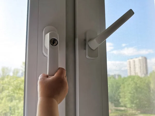 A children\'s hand is trying to open a window with a lock on the handle in an apartment on a high floor. A security lock for windows ensures the safety of your children and prevents accidents.