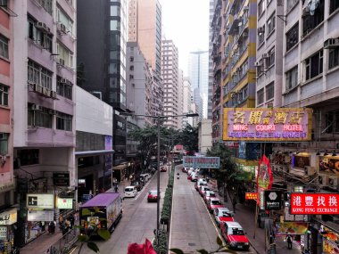 Hong Kong 'da Wan Chai bölgesinin bir caddesini görüyoruz. Şehir taksi ve otobüsleri, otel ve restoran tabelaları, yüksek binalar..