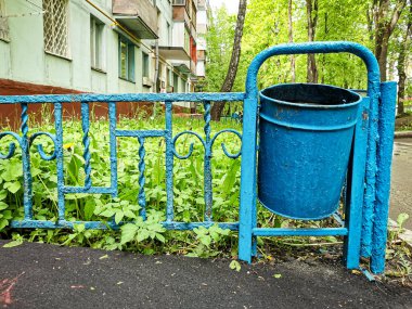Bir konut binasının çıkışındaki alçak çitin yanındaki mavi metalik çöp kutusuna yakın plan. Kentsel altyapı yenileme kavramı.