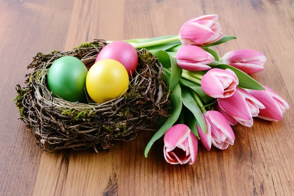 Nid d'œufs de Pâques entouré d'un bouquet de tulipes roses fraîches — Photo