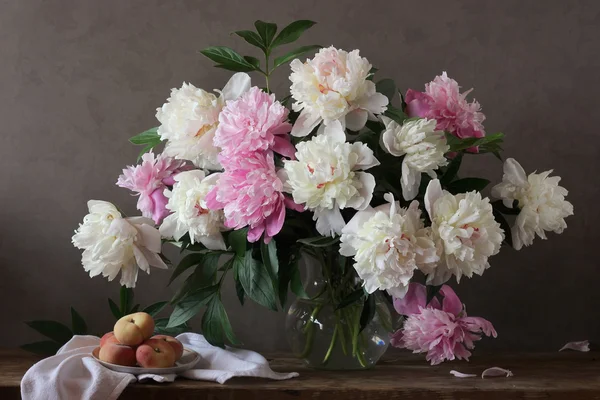 Still-life with a bouquet of peonies and peaches. — Stock Photo, Image