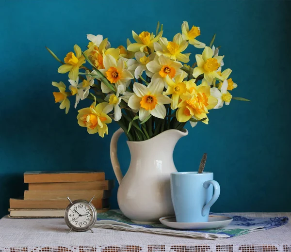 Kytice ze žlutých narcisů v bílém džbánu, budík a knihy — Stock fotografie