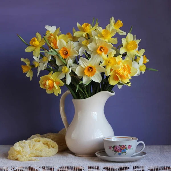 Narcisos em um jarro branco e uma xícara retro na mesa — Fotografia de Stock