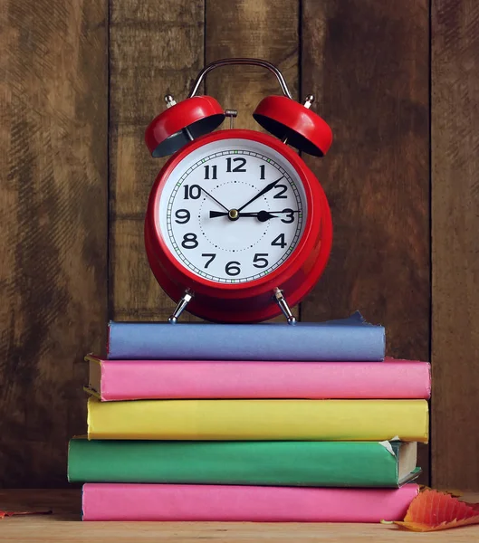 Στοίβα από βιβλία και κόκκινο ρολόι συναγερμών πάνω στο τραπέζι. Επιστροφή στο σχολείο. — Φωτογραφία Αρχείου