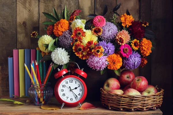 Reloj despertador, ramo, manzanas en cesta y libros sobre la mesa. R — Foto de Stock