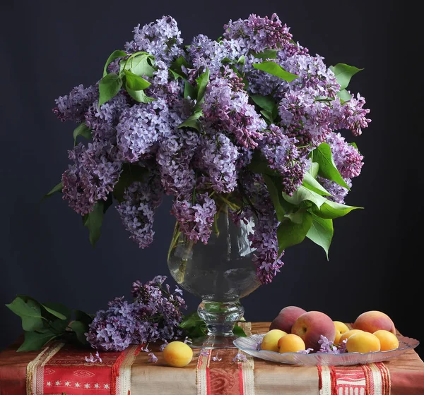 Stilleben med syrener i en vas och frukt — Stockfoto