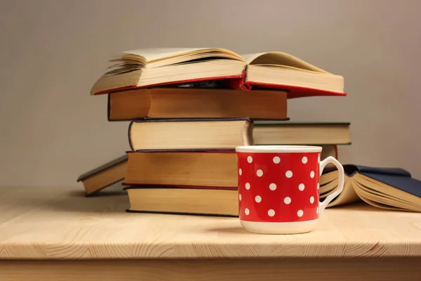 Filiżanka ceramiczna czerwona i stos książek na drewnianym stole. — Zdjęcie stockowe