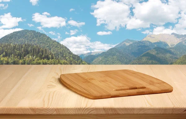 Ξύλινο τραπέζι με την κοπή του σκάφους με φόντο βουνά. — Φωτογραφία Αρχείου