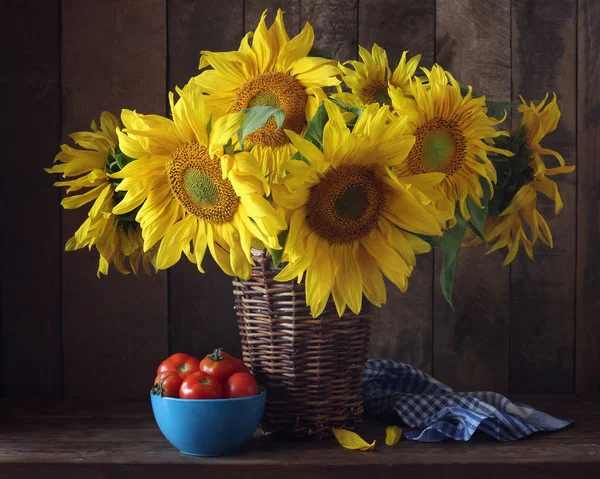 Zonnebloemen in een mand en tomaten op tafel. — Stockfoto