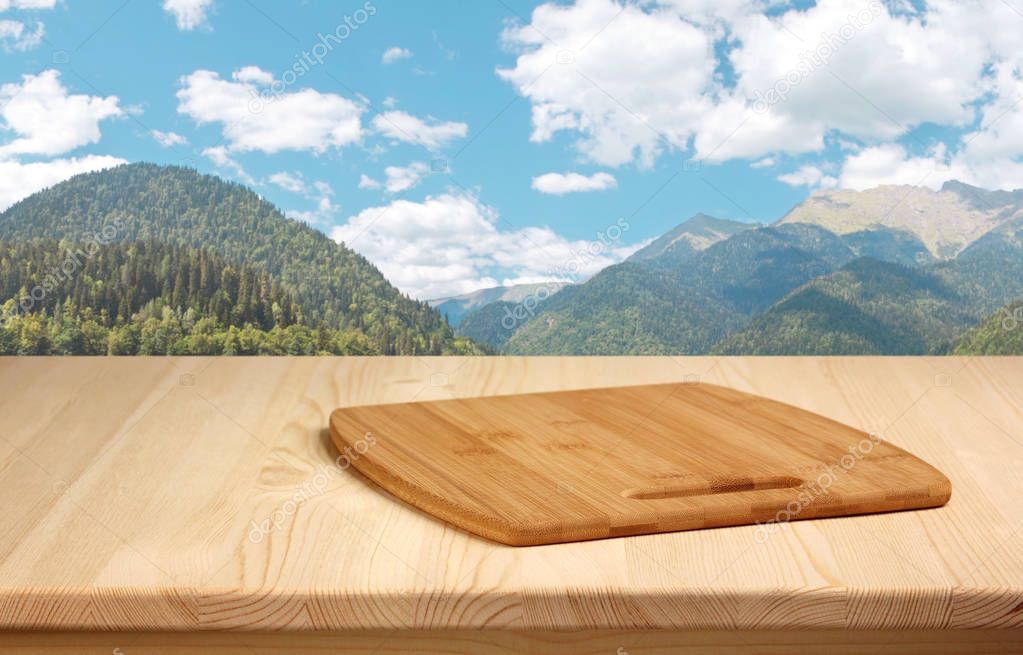 wooden table with cutting Board on a background of mountains.