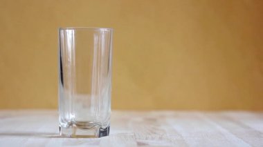 Ahşap bir masa üzerinde bir boş bardak duran içine temiz su akar.