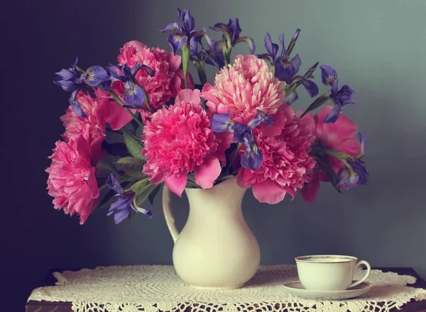 Peonías rosadas e iris en una jarra blanca. naturaleza muerta retro . — Foto de Stock