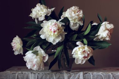 Koyu arkaplanda cam bir vazoda beyaz şakayık demeti.