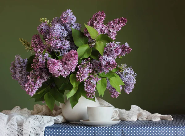 Lila púrpura en una jarra blanca y una taza sobre la mesa . —  Fotos de Stock