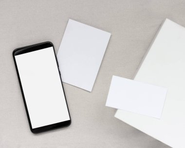 Model, boş kartvizitleri, kartviziti ve hafif tekstil arka planında akıllı telefonu olan bir düzen. düz yatış, üst görünüm.