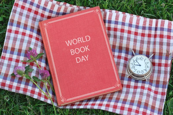 world book day. book with red cover on the grass, top view. outdoor reading, summer vacation.