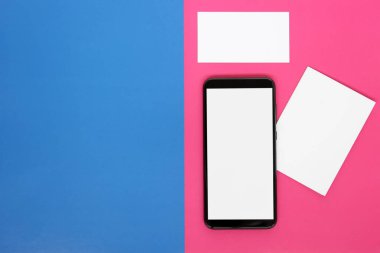 Beyaz ekranlı modern akıllı telefon, beyaz kart ve parlak pembe ve mavi arkaplanlı kartvizit, üst manzara. Metnin için boşluk.