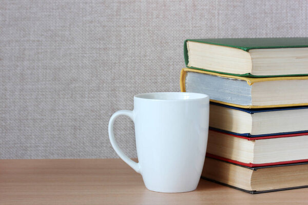 stack of color covered books and a white mug on the table. empty space for Your text or pattern.
