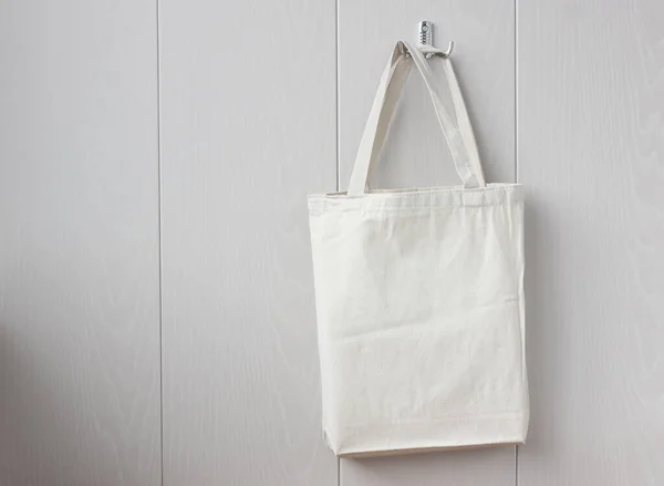 white linen bag hanging on a hook on a light wall. space for your image or text. eco bag.