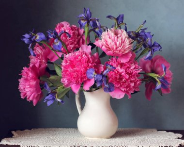 Beyaz bir sürahi içinde bir buket şakayık ve süsen çiçeği. Pembe şakayıklar, bahçe çiçekleri.