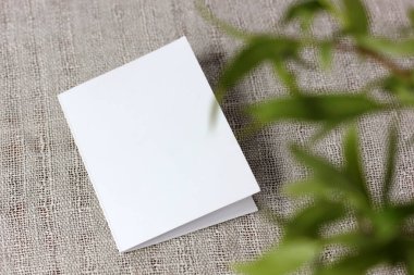 Açık keten bir masa örtüsü üzerinde boş beyaz kart ve bulanık taze yapraklar, üst manzara. Doğal doğal arka plan. Model yap, düzen.
