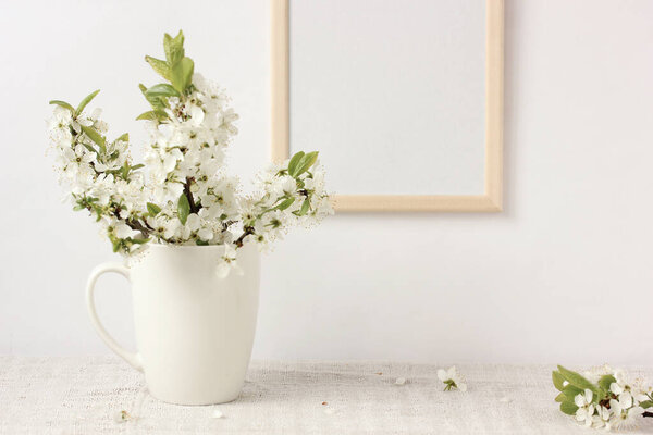 blooming plum branches with white flowers in a Cup and an empty wooden frame with space to copy. tender spring light background, layout, mock-up. place for editing your text or image.