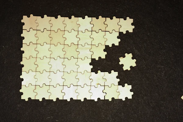 Half ordered puzzle with white jigsaw pieces. One side of the image shows part of the completed puzzle, other side shows the work in progress on a texture black background