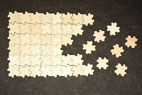 Half ordered puzzle with white jigsaw pieces. One side of the image shows part of the completed puzzle, other side shows the work in progress on a texture black background