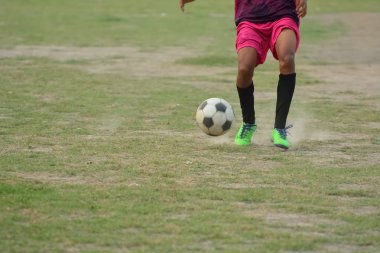 Futbol oyuncusu sahadaki futbol antrenmanı sırasında futbol topunu tekmelemek için koşuyor.