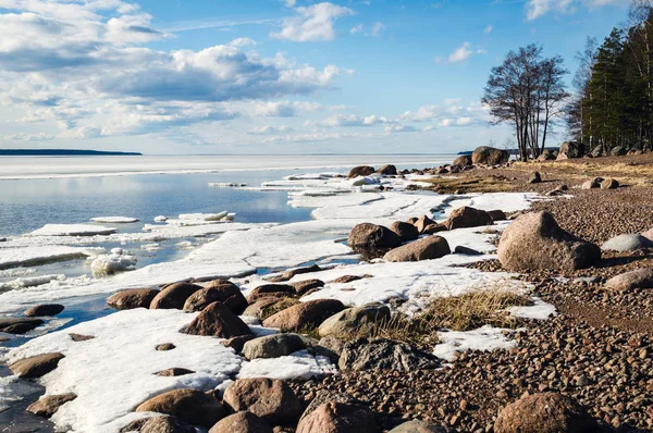 Kar ve buz, mavi bulutlu gökyüzü, orman ve kayalar, güneşli bahar lake shore yatay.