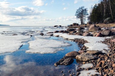 Kar ve buz, mavi bulutlu gökyüzü, orman ve kayalar, güneşli bahar lake shore yatay.