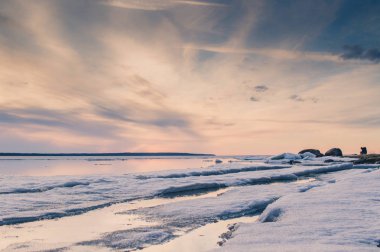 Gün batımını soyut resim göle erken ilkbaharda eriyen buz ile. Altın saat renkler, çim ve taşlar. Bir adam uzakta silüeti