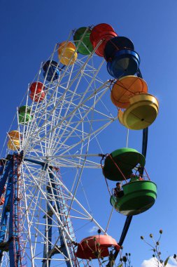 Renkli dönme dolap üzerinde kırmızı, yeşil, mavi ve sarı kabinleri açık mavi gökyüzü