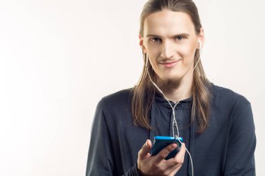 Yakışıklı genç gülümseyen adam onun smartphone cep telefonu ile müzik dinlemek ve beyaz arka plan üzerinde kamera arıyorum. Yaşam tarzı insan ve teknoloji kavramı.