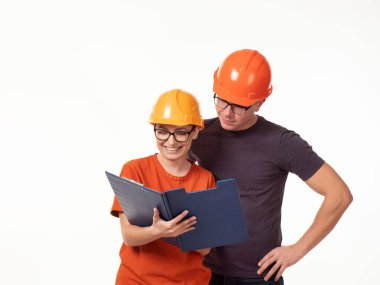 Duygusal, genç. Yanında kadın ustabaşı olan, gözlüklü ve elinde beyaz bir arkaplan olan sarı kasklı bir adam.