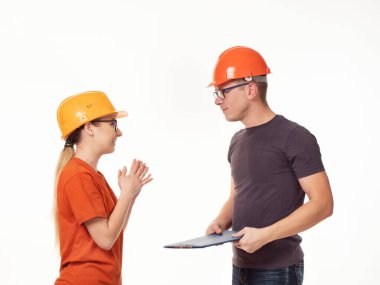 Duygusal, genç. Yanında kadın ustabaşı olan, gözlüklü ve elinde beyaz bir arkaplan olan sarı kasklı bir adam.